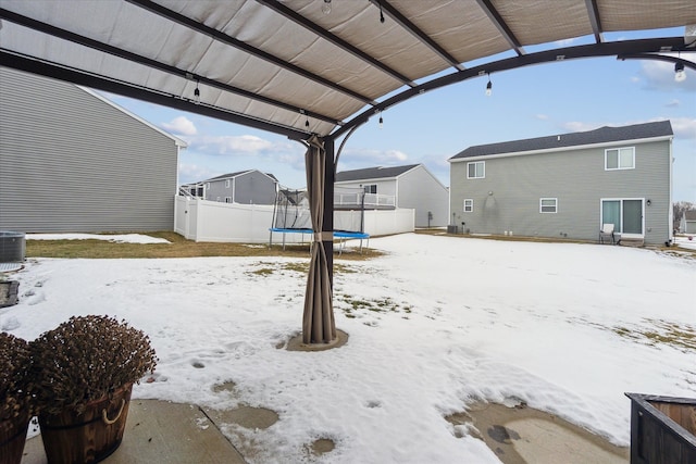 snowy yard featuring a trampoline and fence