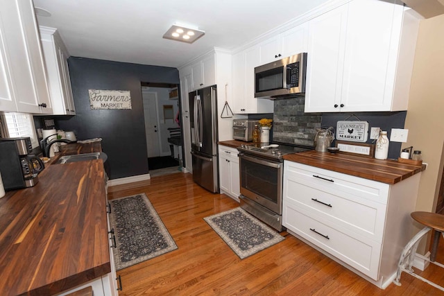 kitchen with light wood-style flooring, a sink, white cabinetry, stainless steel appliances, and wooden counters