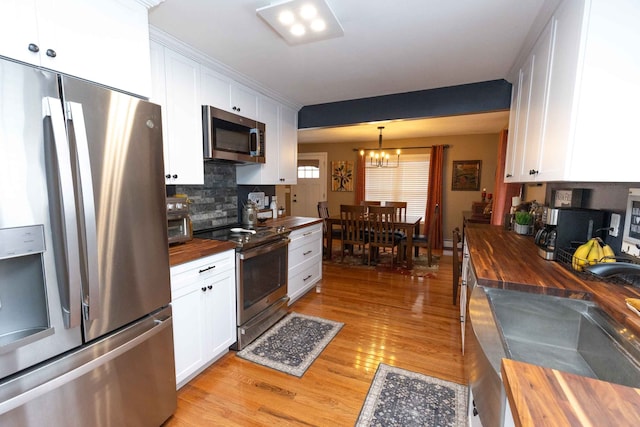 kitchen featuring light wood finished floors, wooden counters, decorative backsplash, appliances with stainless steel finishes, and white cabinets