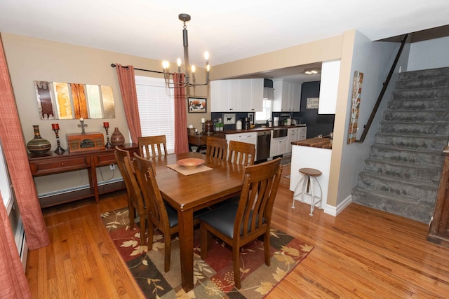 dining area featuring a notable chandelier, light wood-style flooring, a baseboard heating unit, stairway, and a healthy amount of sunlight