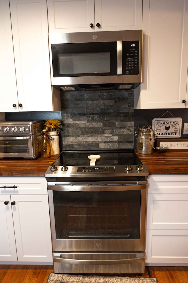 kitchen featuring butcher block countertops, appliances with stainless steel finishes, white cabinets, a toaster, and decorative backsplash