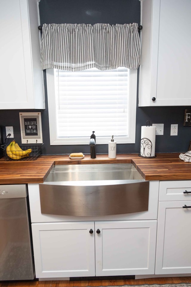 kitchen with a sink, stainless steel dishwasher, butcher block countertops, and white cabinetry