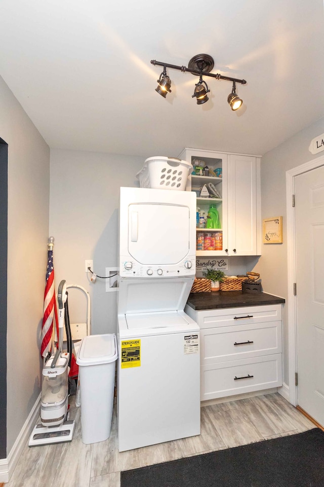 laundry room with track lighting, baseboards, stacked washer and dryer, light wood-style floors, and cabinet space