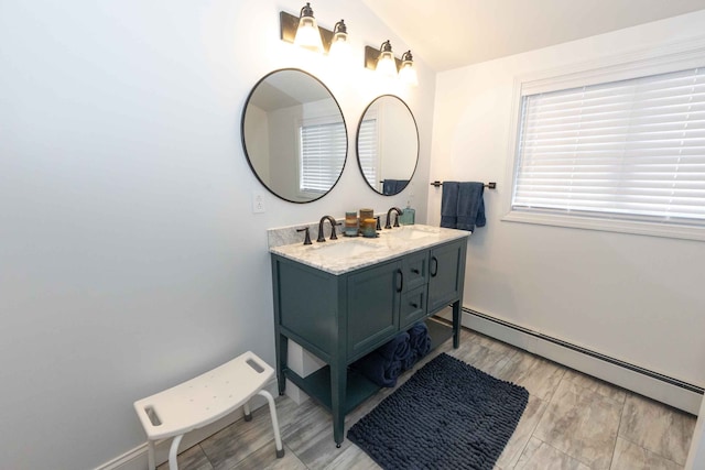 full bath featuring wood finished floors, baseboards, double vanity, a sink, and a baseboard heating unit