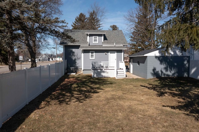 back of house with a lawn, roof with shingles, an outdoor structure, and fence