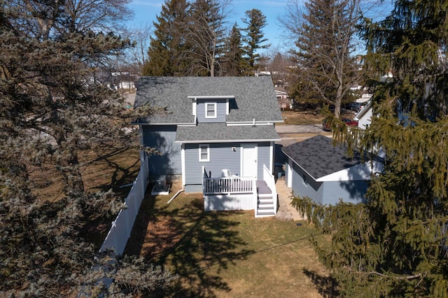 view of front of home with a front yard, fence, roof with shingles, and a wooden deck