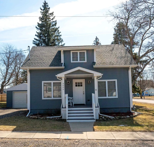 bungalow-style home featuring an outdoor structure, a detached garage, driveway, and a shingled roof