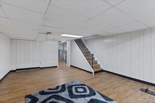 finished below grade area featuring stairs, a drop ceiling, baseboards, and wood finished floors