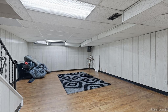 finished below grade area featuring stairway, visible vents, a drop ceiling, and wood finished floors