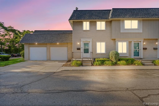 view of front of property featuring mansard roof, an attached garage, a shingled roof, brick siding, and driveway