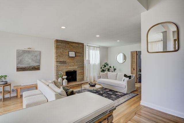 living area with light wood-style floors, recessed lighting, a stone fireplace, and baseboards