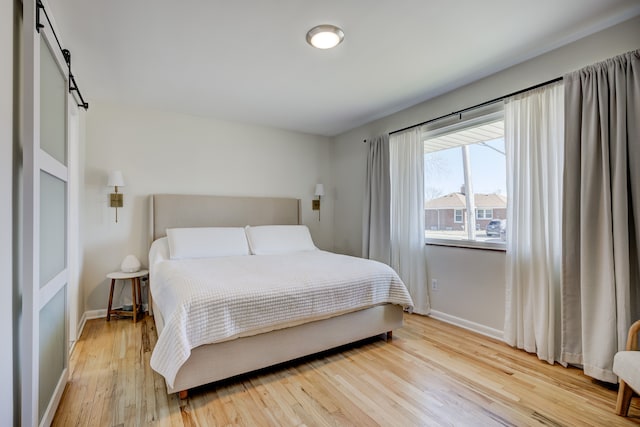 bedroom featuring light wood finished floors, a barn door, and baseboards