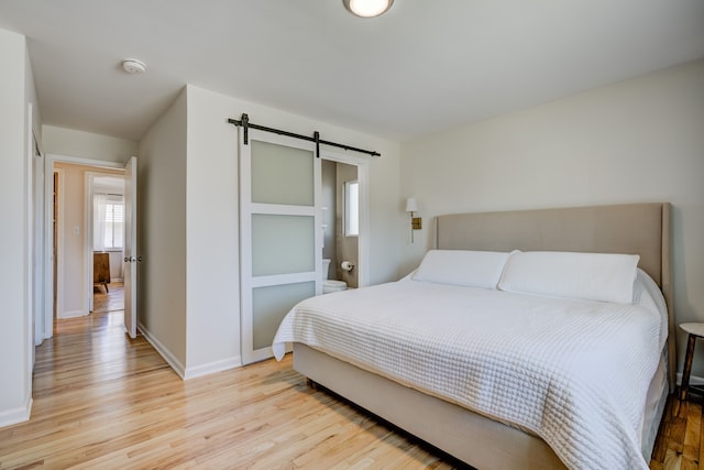 bedroom featuring light wood-style floors, baseboards, and a barn door