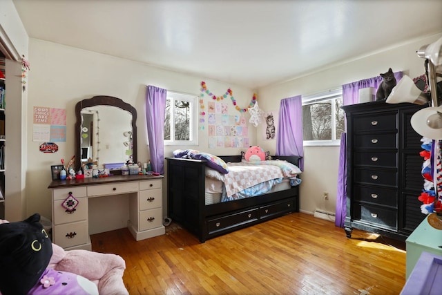 bedroom with light wood finished floors, multiple windows, and a baseboard heating unit