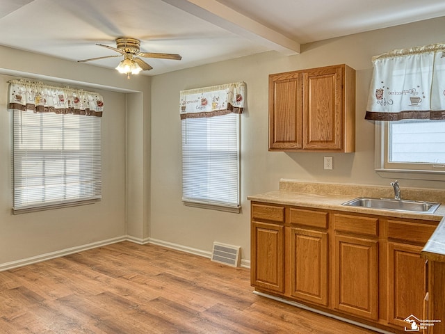 kitchen with light wood finished floors, visible vents, beamed ceiling, light countertops, and a sink