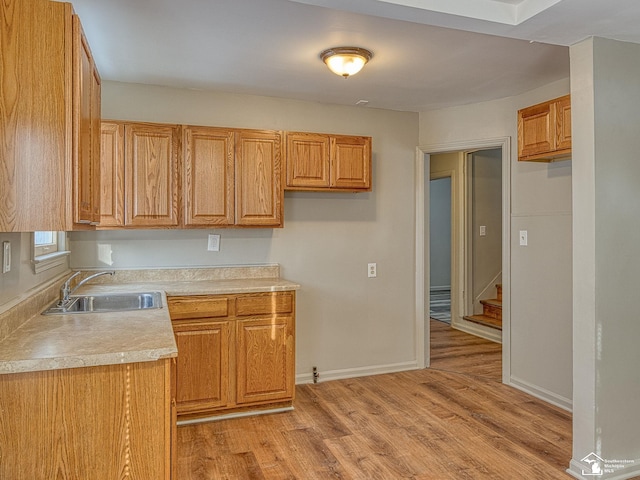 kitchen featuring light countertops, a sink, light wood-style flooring, and baseboards