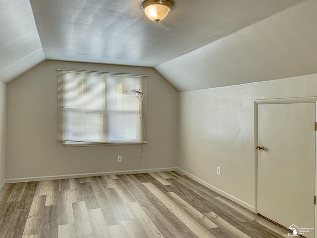 bonus room with light wood finished floors, baseboards, and vaulted ceiling