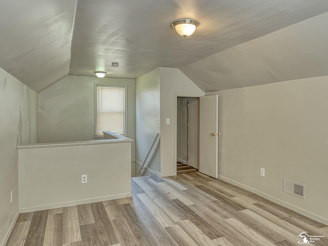 additional living space with vaulted ceiling, baseboards, visible vents, and light wood-style floors