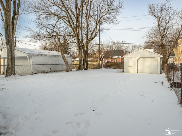 yard covered in snow featuring a garage, an outdoor structure, and fence