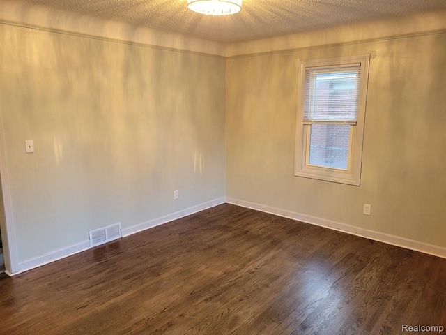 empty room featuring a textured ceiling, dark wood-type flooring, visible vents, and baseboards