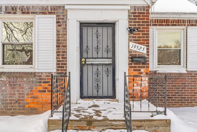 snow covered property entrance featuring brick siding