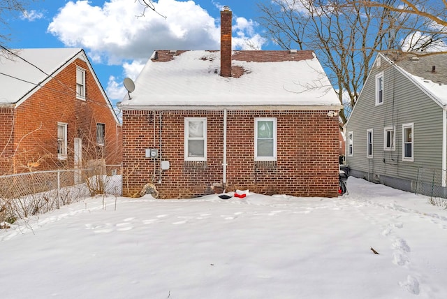 snow covered rear of property featuring brick siding, fence, and a chimney