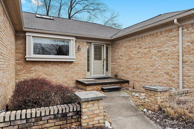 entrance to property featuring roof with shingles and brick siding