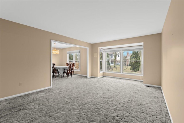 empty room with an inviting chandelier, visible vents, baseboards, and carpet flooring