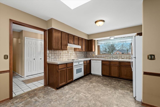 kitchen with white appliances, tasteful backsplash, tile counters, under cabinet range hood, and a sink