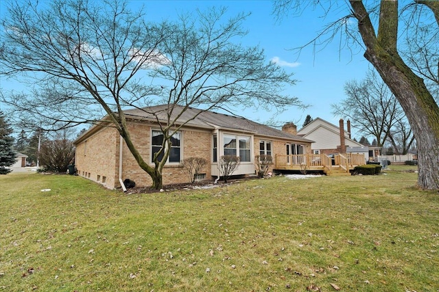 back of house featuring a chimney, brick siding, a yard, and a deck