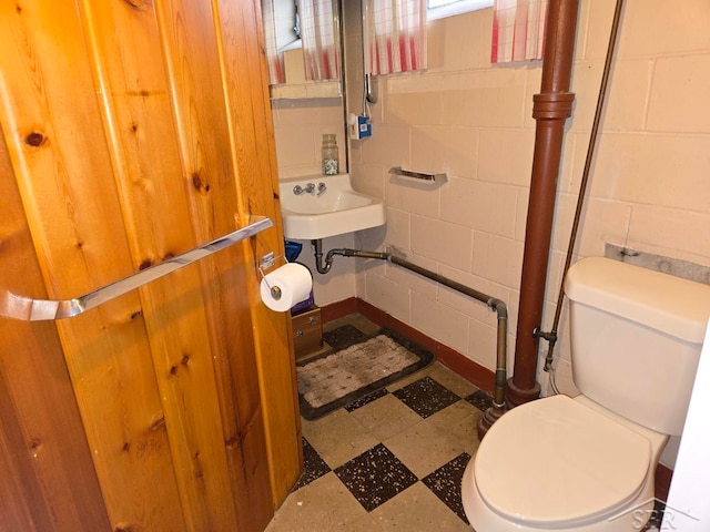 half bathroom featuring concrete block wall, a sink, toilet, and tile patterned floors