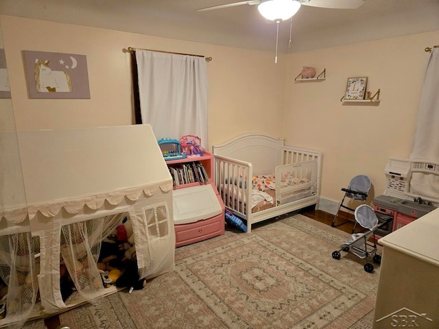 bedroom with a crib, a ceiling fan, and wood finished floors