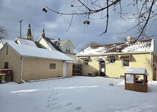 snow covered rear of property with brick siding