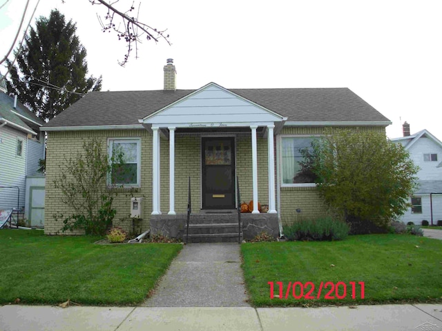 bungalow featuring roof with shingles, a chimney, a front lawn, and brick siding