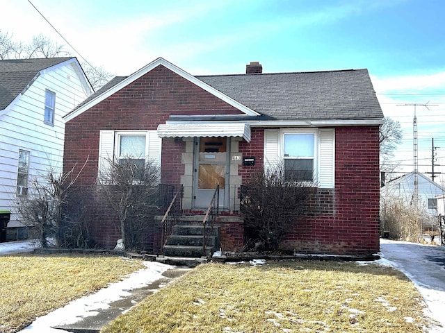 bungalow-style house with a chimney, a front lawn, and brick siding