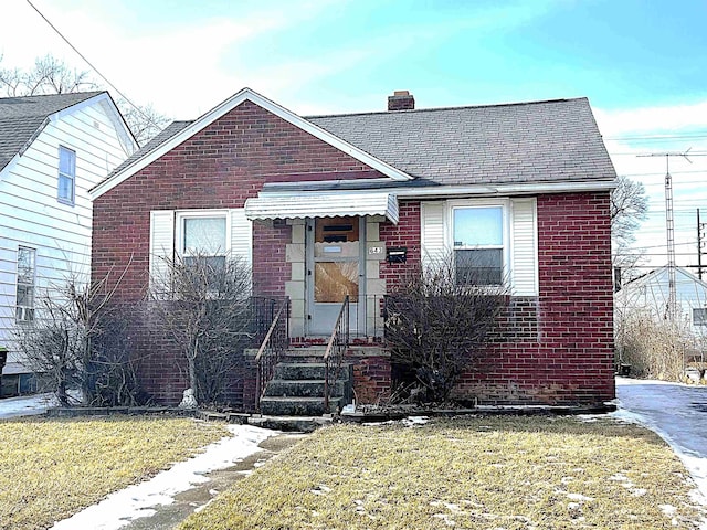 bungalow-style house featuring brick siding, a chimney, and a front yard