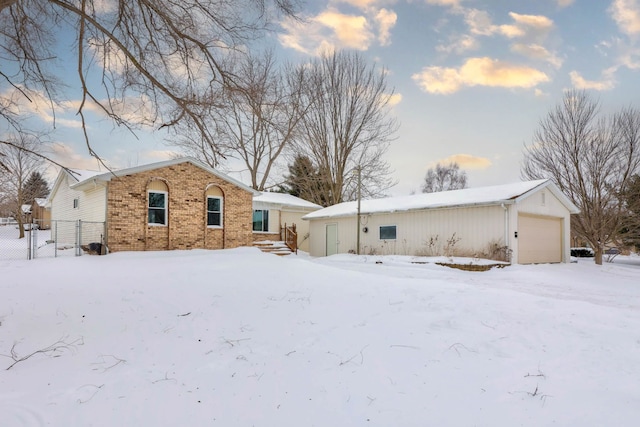 snow covered property featuring an outbuilding, a garage, fence, and brick siding