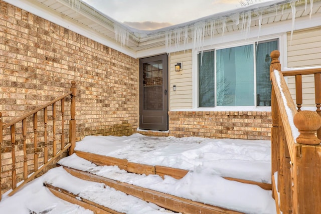 snow covered property entrance featuring brick siding