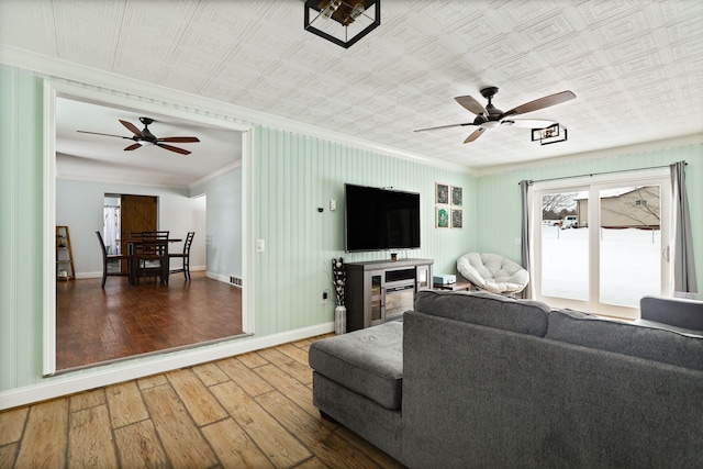 living area featuring wood finished floors, visible vents, baseboards, a ceiling fan, and crown molding