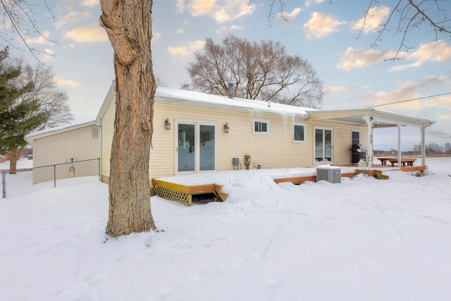 snow covered rear of property featuring central AC and fence