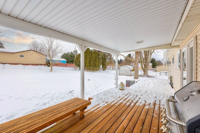 snow covered deck with fence, an outdoor structure, and a storage unit