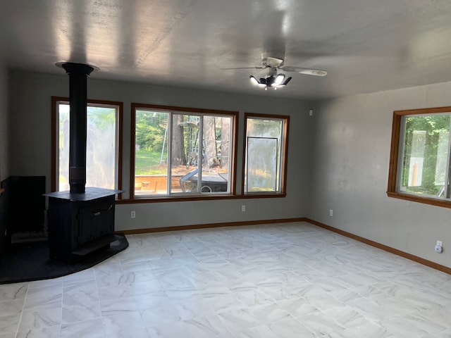 living room featuring a ceiling fan, a wood stove, and baseboards