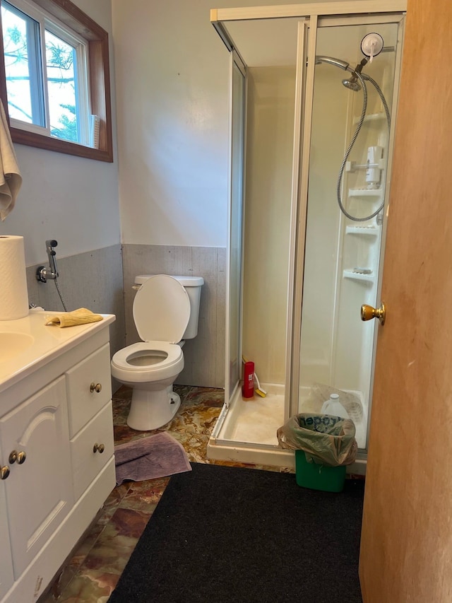 bathroom with a wainscoted wall, toilet, a shower stall, and vanity