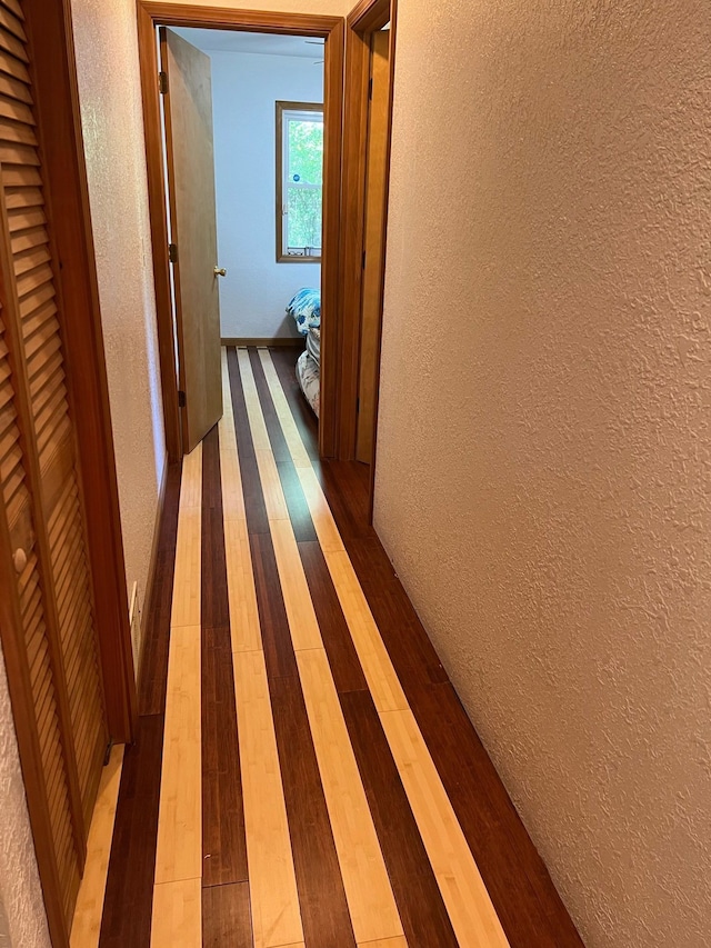 corridor with a textured wall and hardwood / wood-style flooring