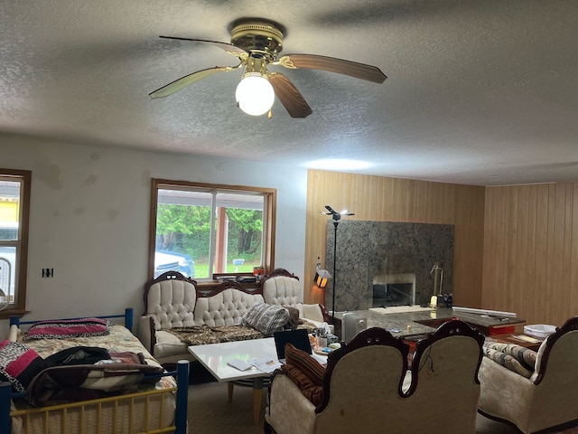 living area featuring a healthy amount of sunlight, ceiling fan, wooden walls, and a textured ceiling
