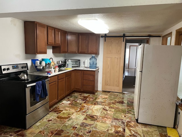 kitchen featuring a textured ceiling, a barn door, light countertops, freestanding refrigerator, and electric stove