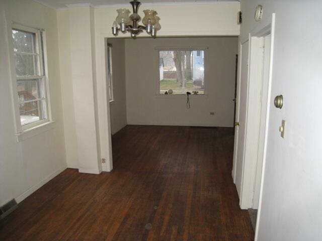 unfurnished dining area with dark wood finished floors, visible vents, and an inviting chandelier