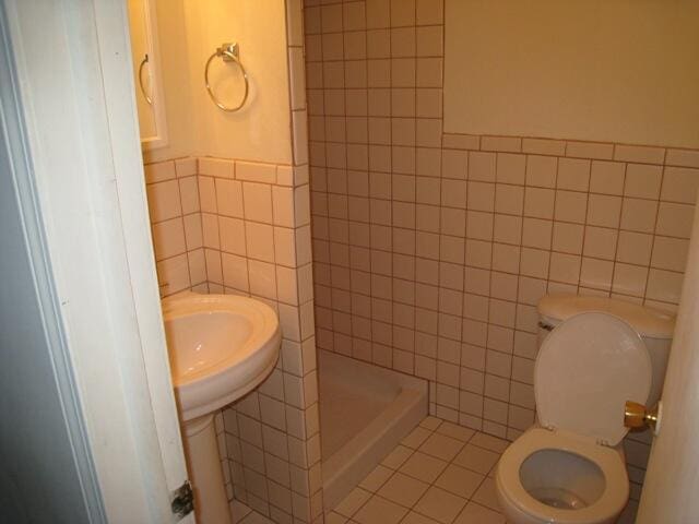 full bath with a stall shower, tile patterned flooring, tile walls, and toilet