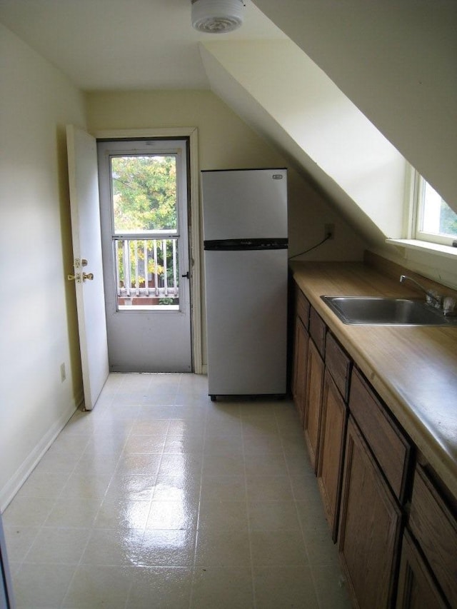 kitchen featuring brown cabinets, lofted ceiling, light countertops, freestanding refrigerator, and a sink