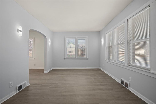 empty room with baseboards, visible vents, arched walkways, and wood finished floors